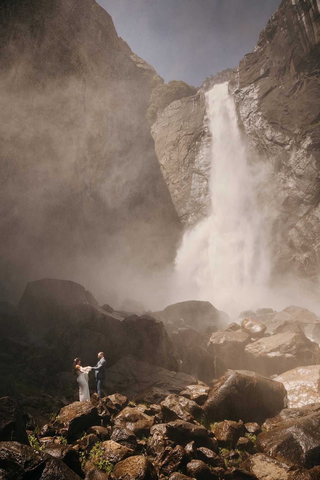 A couple stands of a portriat together at the base of Yosemite Falls.