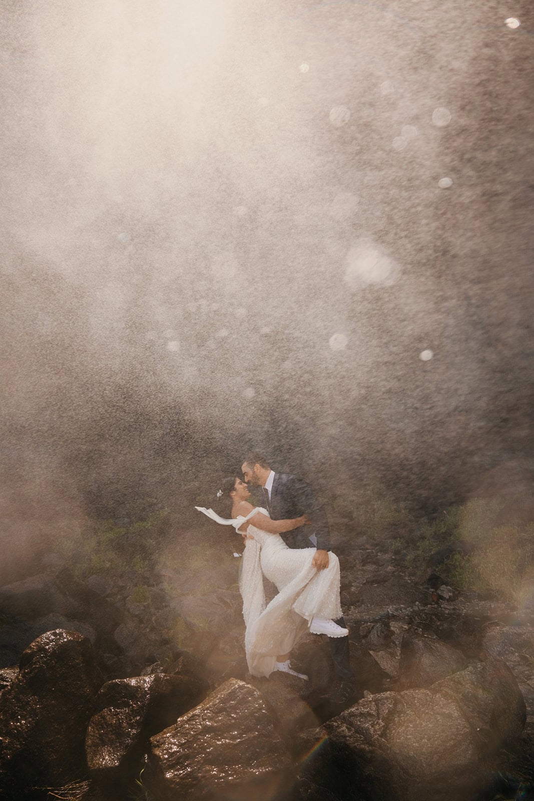A couple romantically embraces in the depths of the powerful waterfall.