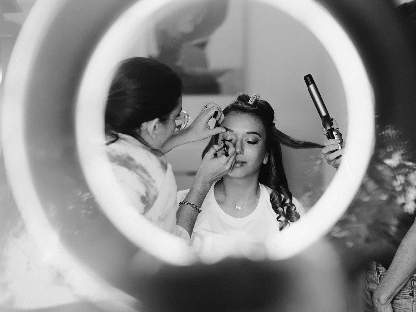 A bride gets her hair and make up done by a stylist.