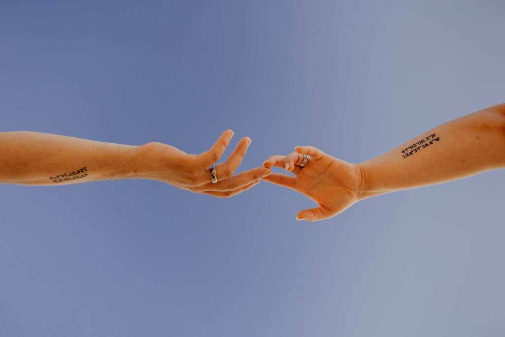 A couple reaches for each other's hands showing off their matching tattoos of the coordinates they got married at.