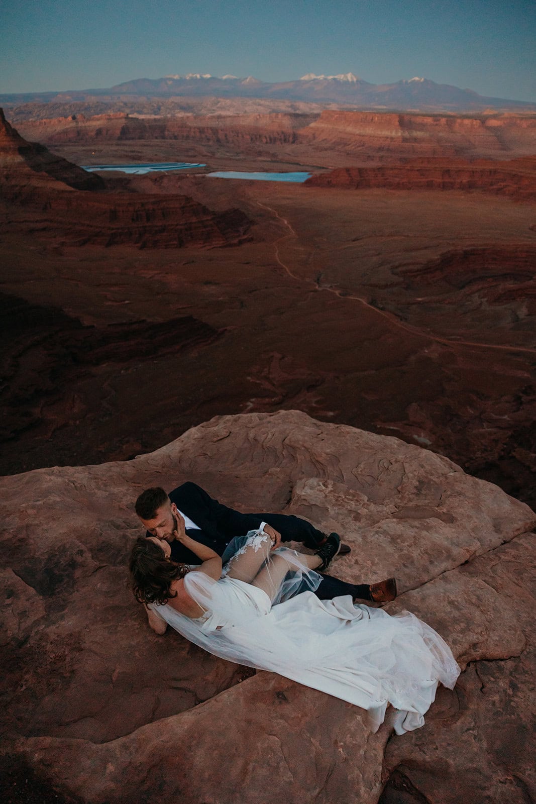 A couple shares a kiss laying on the sand stone rocks of Moab at dusk.