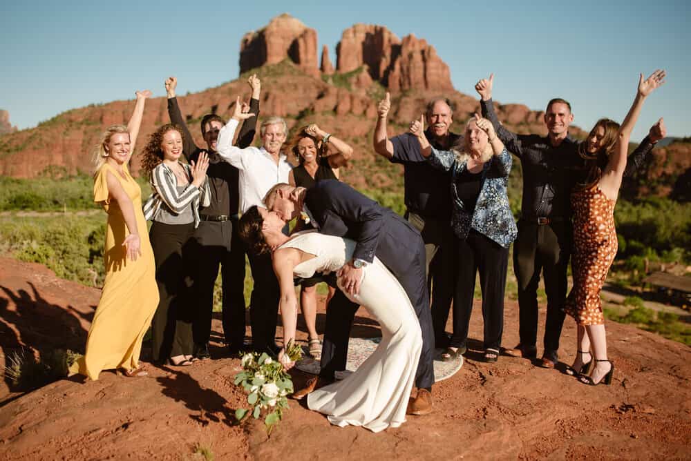 The groom dip kisses the bride as the family celebrates all around them.