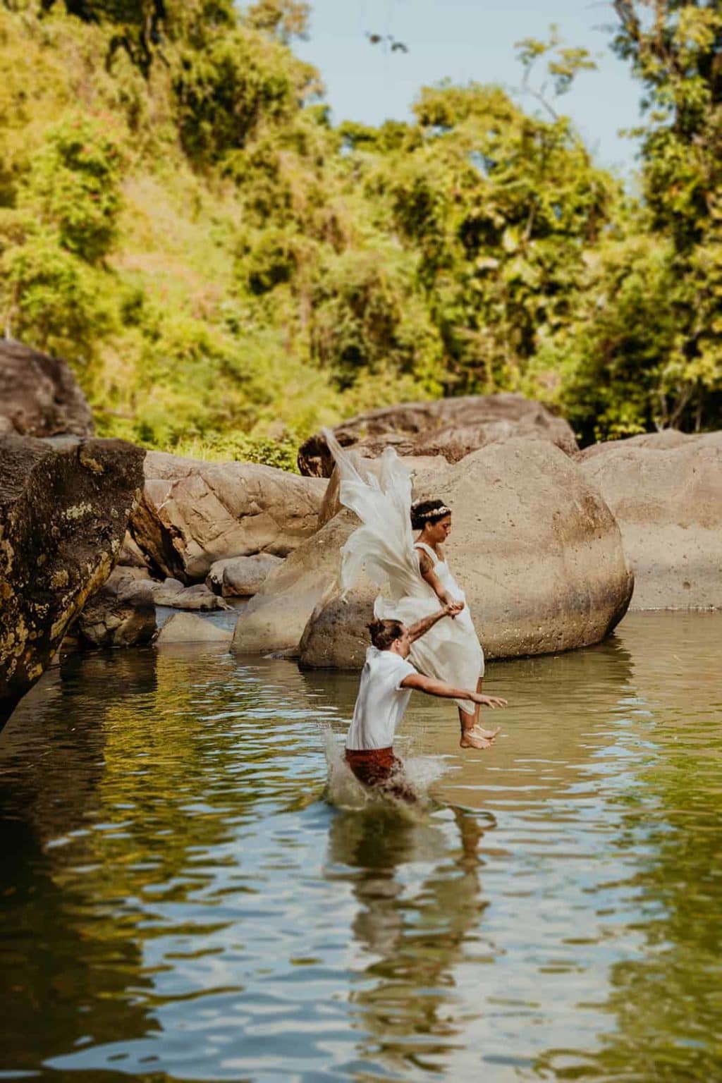 A couple jumps into a river wearing their wedding attire.
