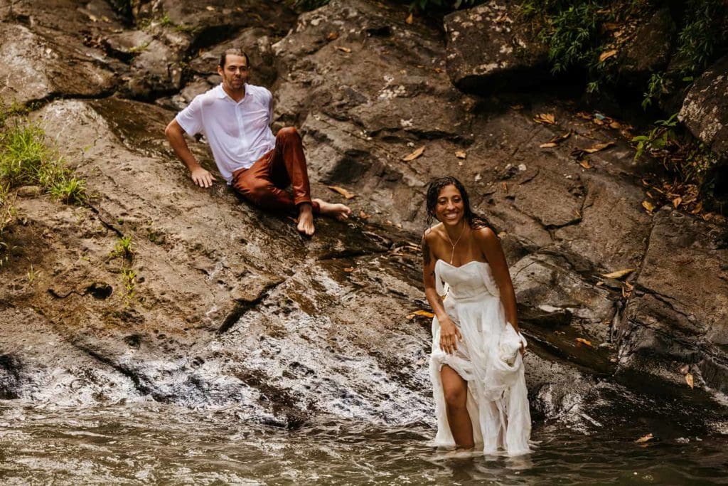 A bride smiling at her friends as she stands in the water wearing her wedding dress. 