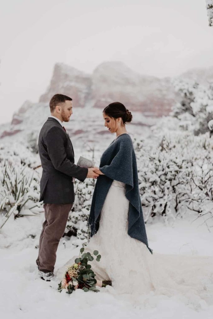 A couple reads their vows to each other in the snow.