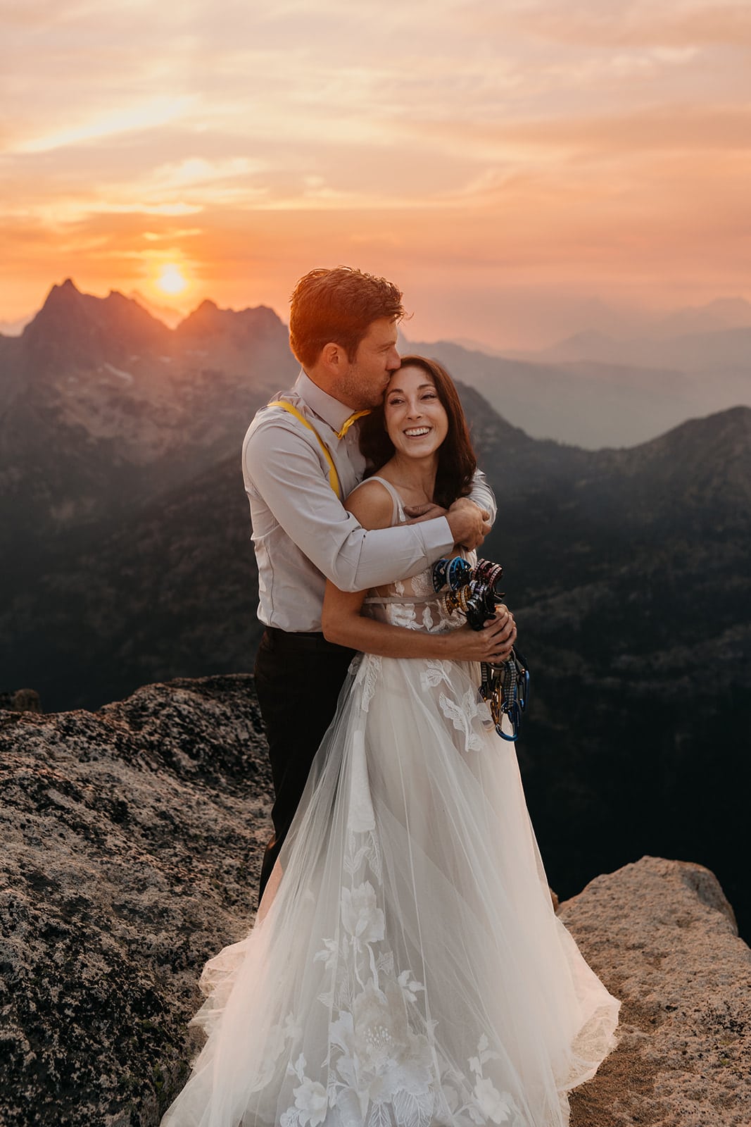 a detail shot of a bride holding climbing cams while her groom hugs her from behind.