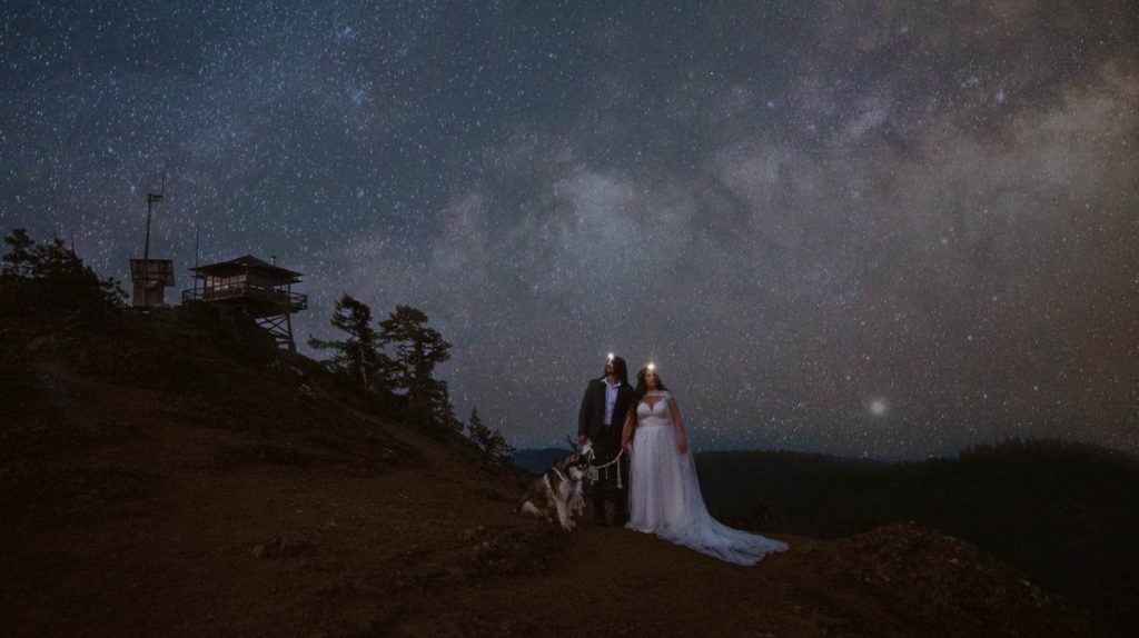 A couple stands under the stars in their wedding attire.