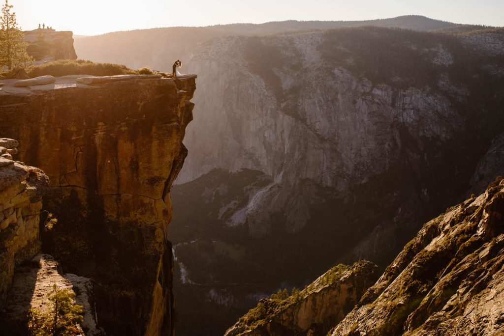 A couple shares a dip kiss at sunset with El Capitan in the background.