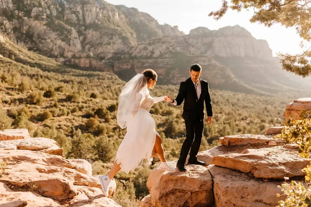 A groom helps his bride cross over a gap between two rocks in Sedona.