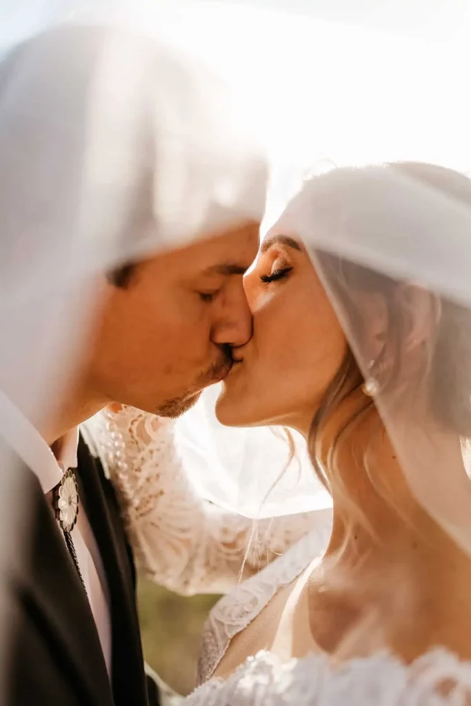 A close up photograph of a bride and groom kissing under a viel.