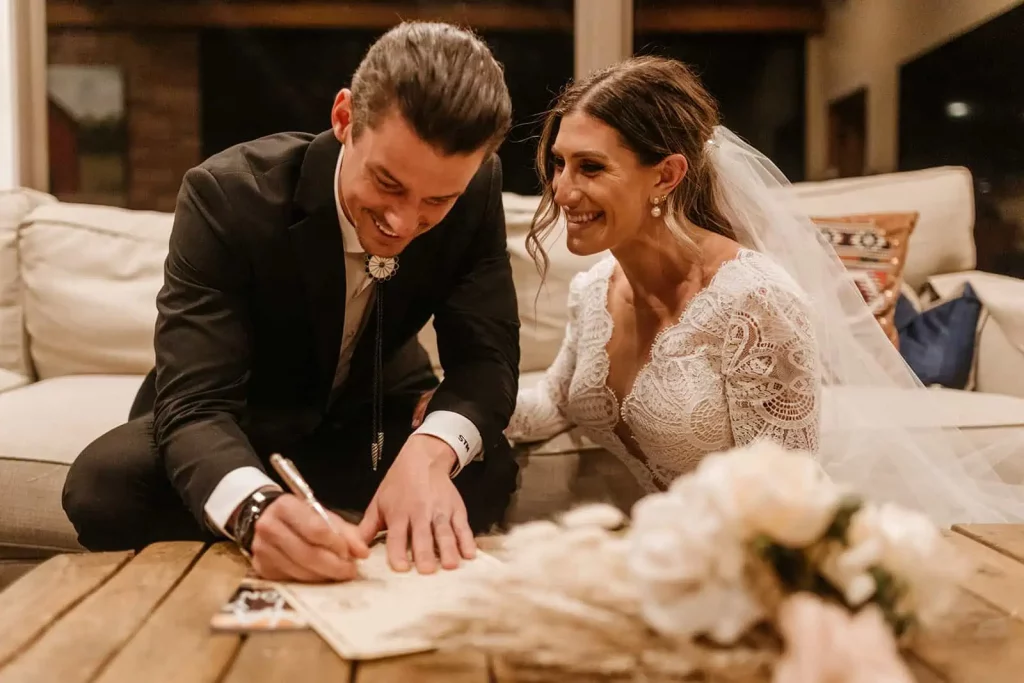 A bride and groom sit together as they sign their marriage paperwork.